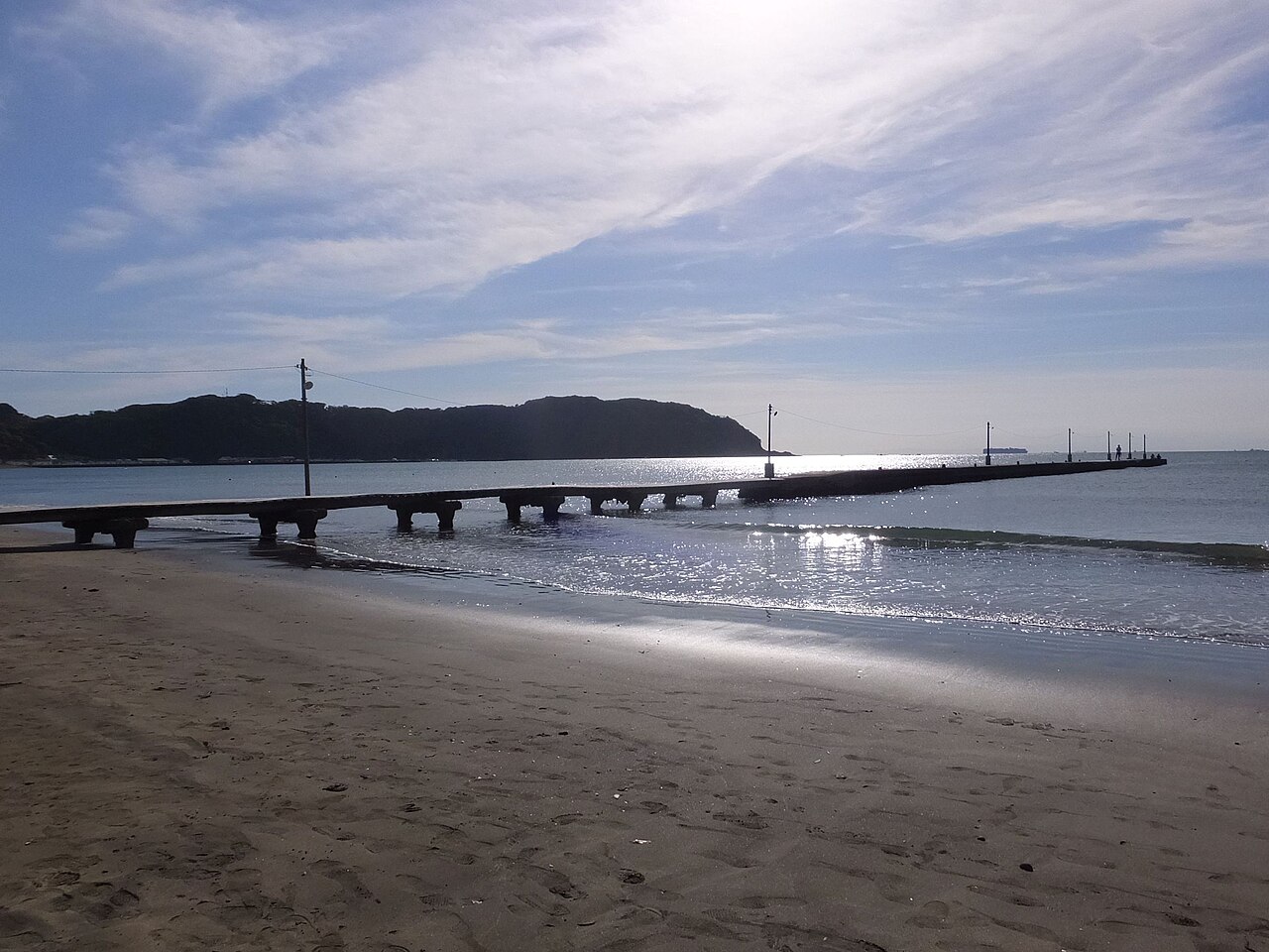 砂浜から海へ延びる原岡桟橋と、桟橋に並ぶ細い電柱。