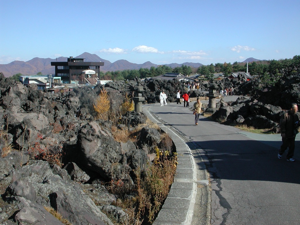 鬼押出し園の黒い溶岩と遊歩道、その向こうに続く山の景色。