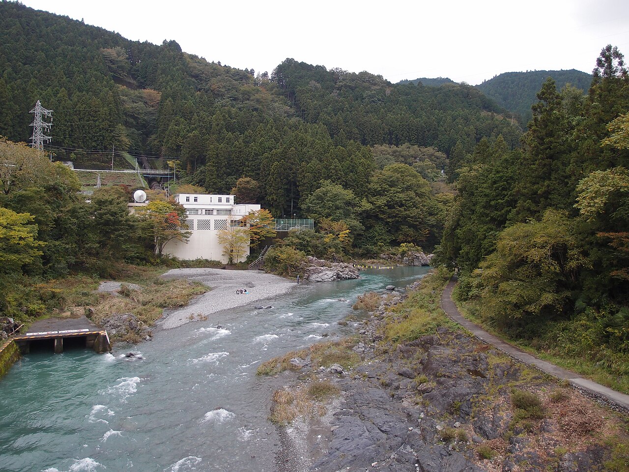 御岳渓谷の多摩川と岩場。両岸の樹木と川沿いの歩道が見える。