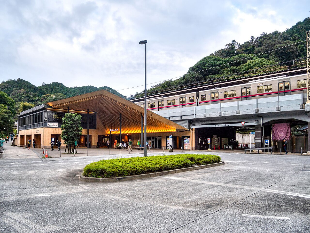 高尾山口駅の木造の屋根と駅前広場。奥に京王線の電車と山が見える。